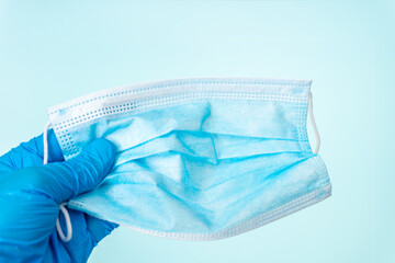Doctor hand wear blue medical gloves holds surgical face mask on blue background. Pandemic concept. Prevent the spread of virus disease. Corona Virus Pandemic. Doctor holds surgical mask in hospital. 