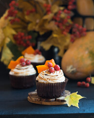 Homemade pumpkin muffins cupcakes decorated with meringue, berries and pieces of pumpkin on black wooden table with autumn leaves in background. Selective focus