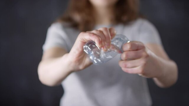 Midsection closeup of plastic water bottle in selective focus and young female activist crumpling it for clear environment