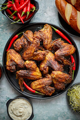 Grilled chicken wings with chilli pepper on a rustic plate served with various dips and bread
