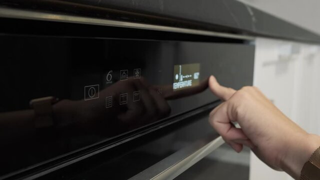 Woman touching sensor button on electric oven in kitchen. Female hand using modern panel of electric oven choosing cooking mode. Close up 4k