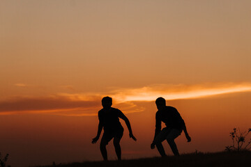 Fototapeta na wymiar Silhouette of two Indian friends jumping with arms raised against the sky during the sunset 