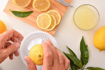 Hands preparing a lemonade squeezing a lemon on bench top