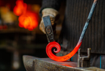 The blacksmith twists the spiral with a sledgehammer, placing a red-hot iron blank on the anvil....