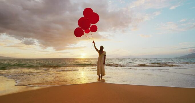 Happy young woman with red balloons on the beach at sunset