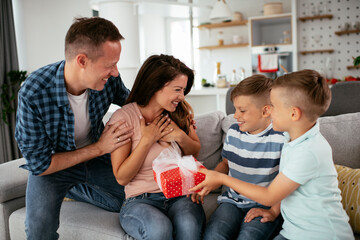 Two young sons are giving their mother a gift. Mother is suprised to receive a present from sons.