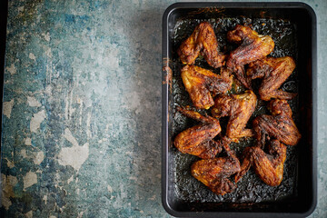 Grilled chicken wings in spices in black metal baking tray on stone table. Top view