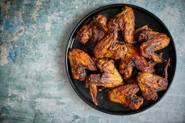 Grilled chicken wings on a black ceramic plate. Placed on a stone
