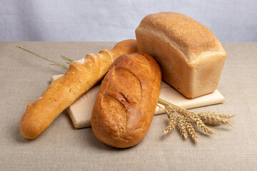 loaf of white bread, baguette and wheat ears on a wooden cutting board