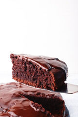 A slice of homemade chocolate cake on a metal spatula vertical on a light background.