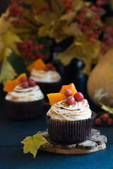 Homemade pumpkin muffins cupcakes decorated with meringue, berries and pieces of pumpkin on black wooden table with autumn leaves in background. Selective focus
