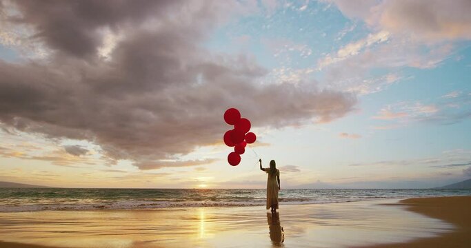 Happy young woman with red balloons on the beach at sunset