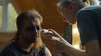 Make-up artist using special equipment applying zombie make up on male face