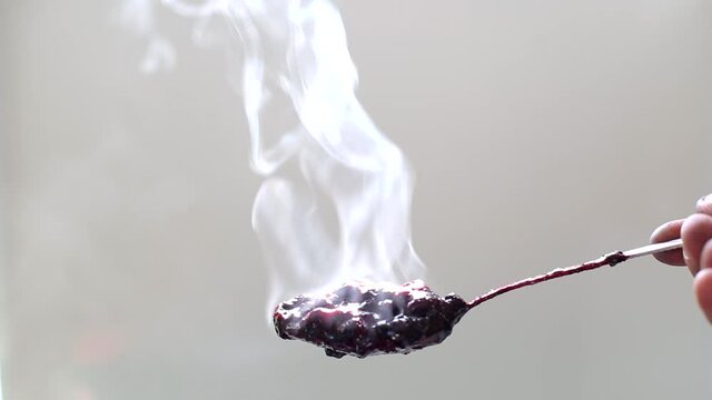 Spoon with hot blueberry jam on the background of the sun, strong steam