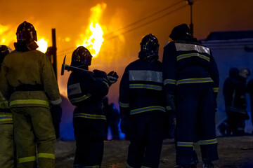 Silhouettes of firefighters against background of burning building. Extinguishing fire.