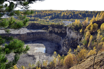 An old stone quarry in a large ravine among the Ural forests in autumn decoration. In the foothills of the Western Urals, golden autumn.