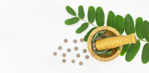 Top view a wooden mortar with pestle with green leaves and natural pills on white background with space for text. banner. dietary food supplement or biologically active additives.