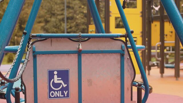 A locked swing for wheelchair users on an empty playground in the rain. Autumn day, yellow leaves on trees, shot from steadicam
