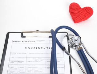 Red knitted heart next to stethoscope and patient examination form