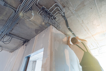 Worker is installing the electrical wires on the ceiling that is the part of internal wiring in...