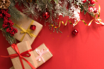 Beautiful Christmas composition with gift box tied with a ribbon, presents and fir branches on red background.