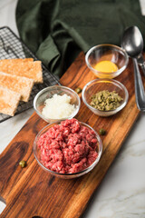 Gourmet Rindertatar Beef Tatar  aus Rindfleisch Filet fettarm  und roh, Kapern, Eigelb, Zwiebeln, Toast Brot auf Holzbrett und Marmor Hintergrund hell