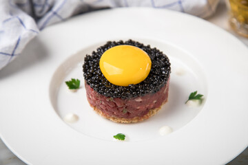 Gourmet Rindertatar Beef Tatar roh aus Filet fettarm, Kapern, Eigelb, Zwiebeln auf Toast Brot und schwarzer Kaviar mit Bier, Küchentuch und Marmor Hintergrund hell
