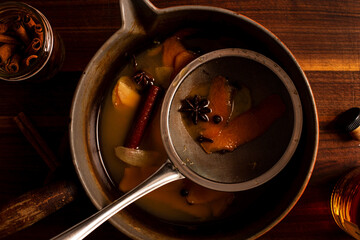 Strainer in a sauce pan of mulled apple cider and orange cocktail.