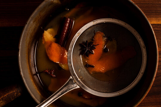 Strainer in a sauce pan of mulled apple cider and orange cocktail.