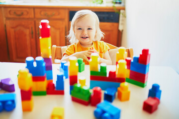 Adorable little girl playing with colorful plastic construction blocks