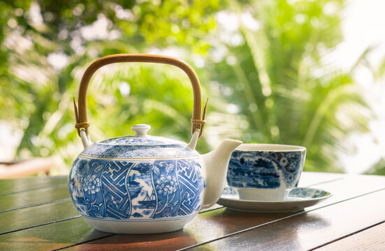 Beautiful blue-patterned white tea set and herbal drinks on a wooden table in a natural setting in the morning.