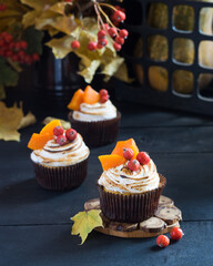 Pumpkin muffins cupcakes decorated with meringue, berries and pieces of pumpkin on black wooden table with autumn leaves in background. Selective focus