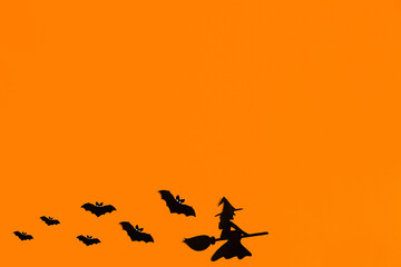 Silhouettes of a flock of bats and a witch flying on a broom made of black paper on an orange background. Halloween greeting template with copy space. Flat lay for your design. ready-made template