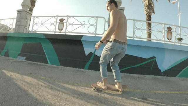 Young boy dressed in jeans without t-shirt skating barefoot along the seaside promenade on a sunny afternoon