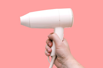 White hair dryer for drying hair in the hands of a man, isolated on a pink background. Beauty salon or hairdresser concept