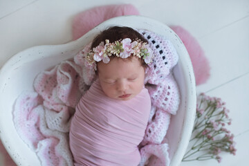 lovely baby girl sleeping in a heart made of wood, wearing hairband decorated with flowers
