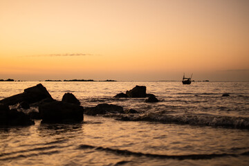 Golden sunset over a beach with rocks and a boat in the waves near Ngwesaung, Myanmar