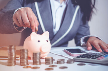 Closeup image businesswoman holding coins putting into piggy bank and calculating. concept saving money wealth for finance accounting.