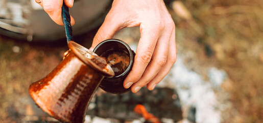 A photo of a man pouring coffee from a turkish coffee pot in a little cup in the morning on field