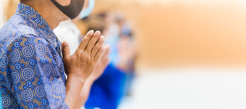 Buddhist senior man with mask praying.male buddhist disciple meditating, prayer hand to the statue of Buddha in temple hall. Abhidhamma pray.Buddhist holidays.Vesak, Pavarana, Anapanasati worship.