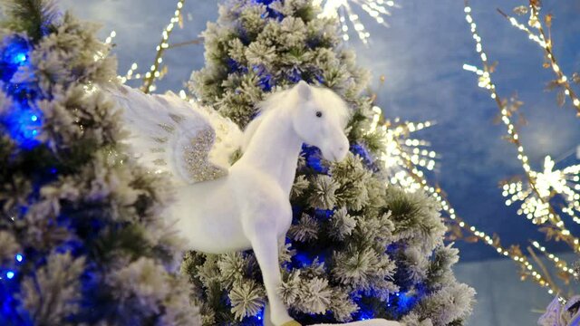 Amazing small white christmas horse with wings among the blue illuminated christmas trees, magic winter decorations and ornaments of polar wildlife thema. Winter christmas magic flying in the air