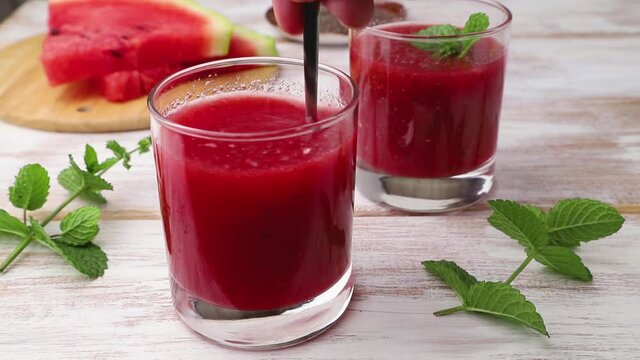 Watermelon juice with chia seeds decorated with mint stir with a spoon in glass on a white wooden background. Healthy drink concept. Side view,  close up.