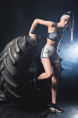Obraz na płótnie Canvas Sportswoman standing near tire in gym with smoke