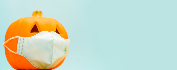 Pumpkin banner blue background.Halloween with mask as a jack o lantern pumpkin wearing a medical face mask protection virus infection coronavirus covid-19.Happy halloween trick or treat.New normal