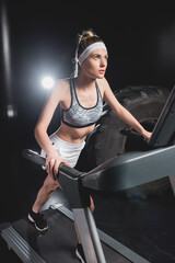 Fototapeta na wymiar Selective focus of young sportswoman running on treadmill near tire in sports center