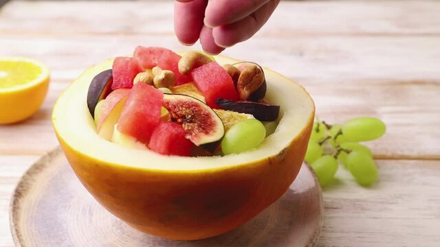 Vegetarian fruit salad of watermelon, grapes, figs, pear, orange on white wooden background decorating with cashew. Side view, close up.
