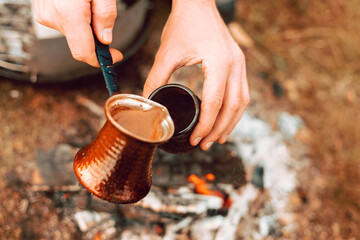 Close up photo on a turkish coffee pot pouring in a cup on a field in the morning - obrazy, fototapety, plakaty