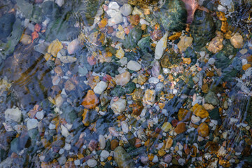 Rocky bottom of mountain stream, close-up. Colorful stones under clear water. Beautiful distortion background. Natural mosaic of small stones. Image for ceramic tile design, bathrooms.