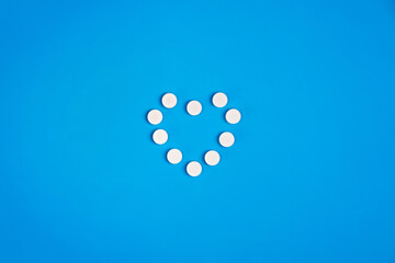 Heart shaped pills on a blue background, top view. Self-care, health care, heart disease concept.