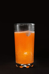 Effervescent tablet of vitamins in a glass of water. Orange antiviral drink. On a black background, close-up.